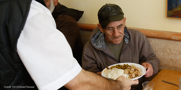 An elderly man being served a plate of food at a restaurant.