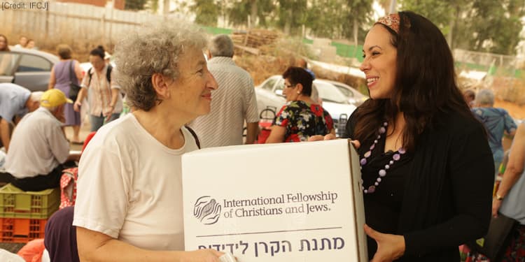 An elderly Jewish woman and Yael Eckstein carrying an IFCJ food box together.