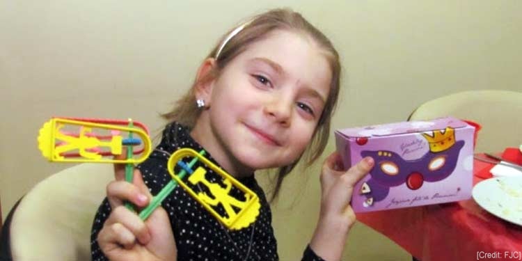 Young girl holding up gifts she received for Purim.