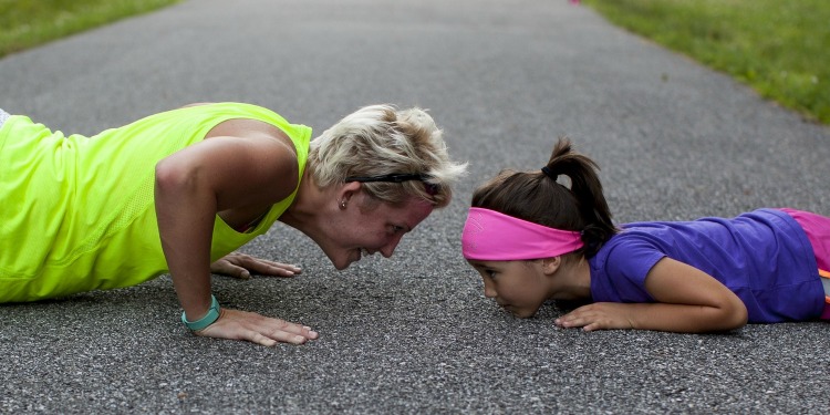 A mom and her daughter doing pushups on a concrete road.