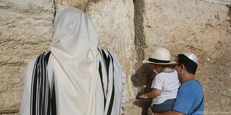 Man dressed in white robe next to a father and his son at the Western Wall.