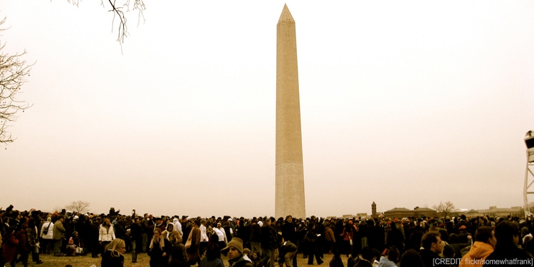 Large crowd gathered around the Washington Monument on a cloudy day.