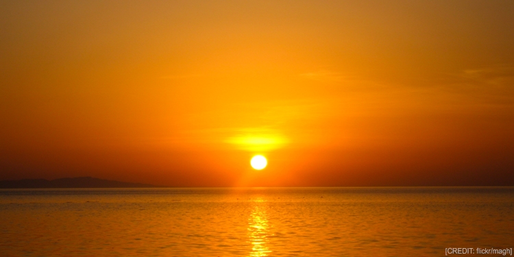 An orange sun set over a large body of water.