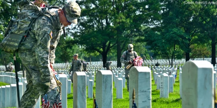 Soldiers walking around a memorial putting flags down at the graves.