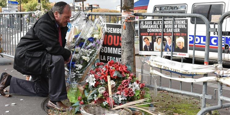 Rabbi Eckstein kneeling in prayer at a memorial with flowers.