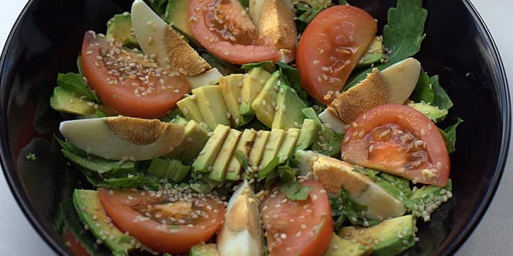 Avocado salad in a black bowl consisting of lettuce, avocado, egg, and tomato.