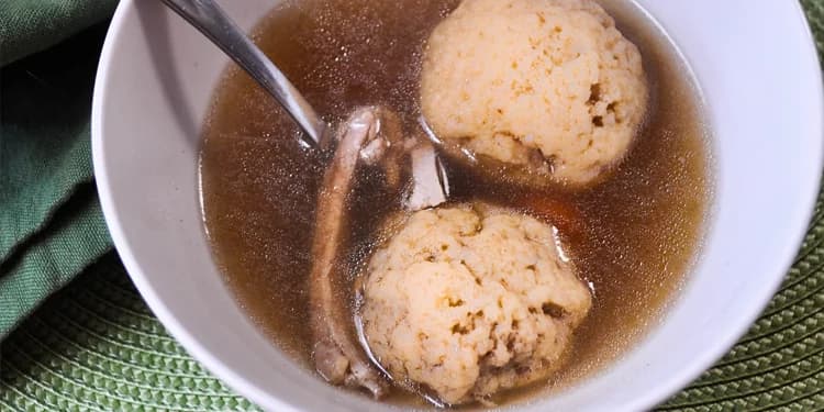 Close up image of matzah ball soup in white bowl.