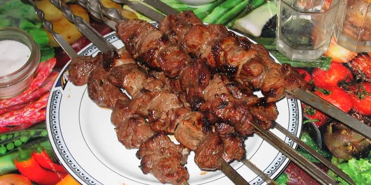 Close up image of four shish-kabobs against a background of vegetables.