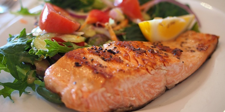 Close up image of salmon on a white plate with a side salad.
