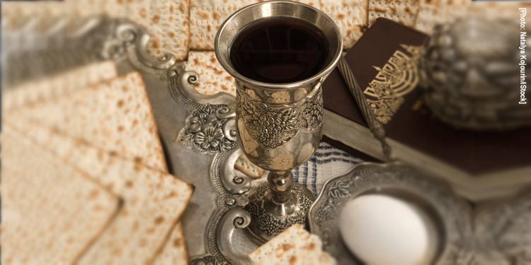 Seder plate with a cup full of juice, egg, matzah crackers and more.