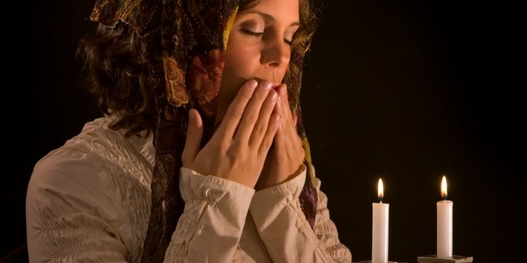 A woman kissing her hands while two candles are below her.