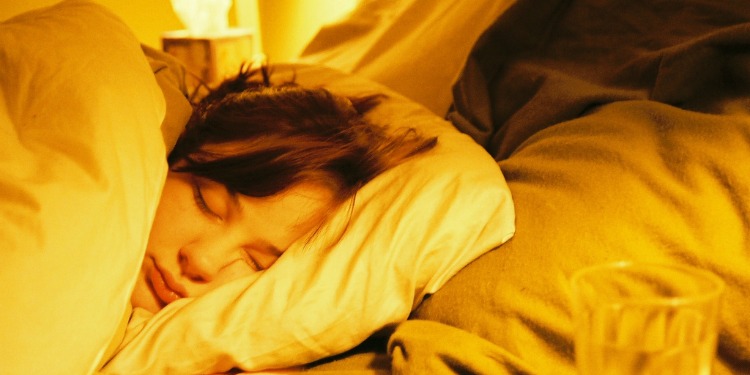 Young woman sleeping with a glass of water beside her bed.