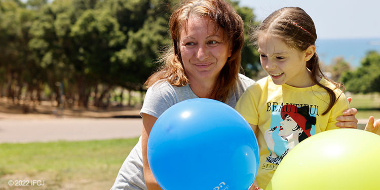 Woman and girl stand in park holding balloons