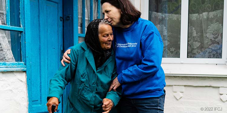 Elderly woman with two canes stands outside with volunteer