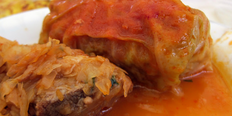 Stuffed cabbage with red sauce on top on a white plate.