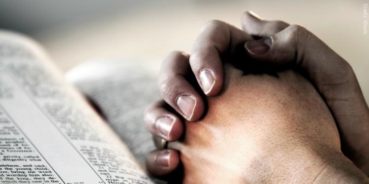 Hands folded in prayer on top of a Bible