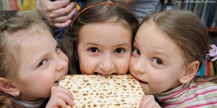 Three young girls biting into a piece of matzah.
