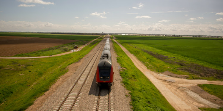 Train passing through on a dirt road in the middle of a green field.