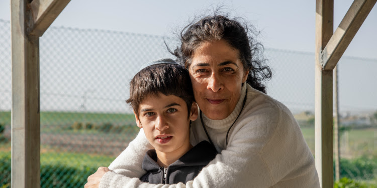 A mother hugging her young son while their standing outside.