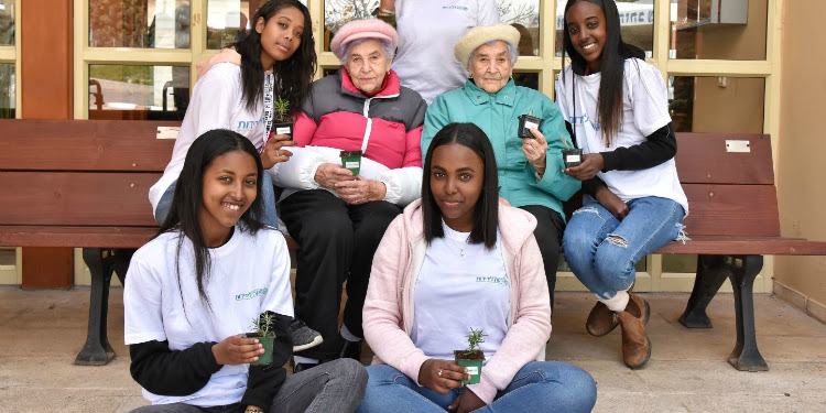Four teenage girls wearing IFCJ shirts spending time with the elderly during Tu B'Shvat.
