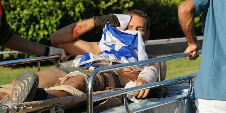 An injured man with the Israeli flag covering him as two medics take him away on a stretcher.