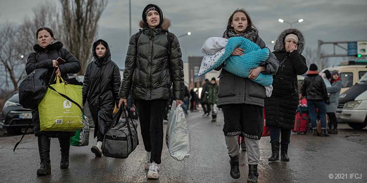 Group of Ukrainian refugees walking down a street carrying luggage
