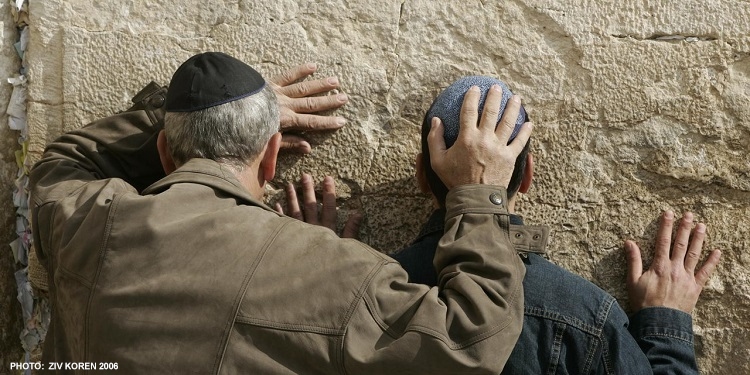 A man and young boy pray to the Western Wall in Jerusalem with their heads pressed against the wall