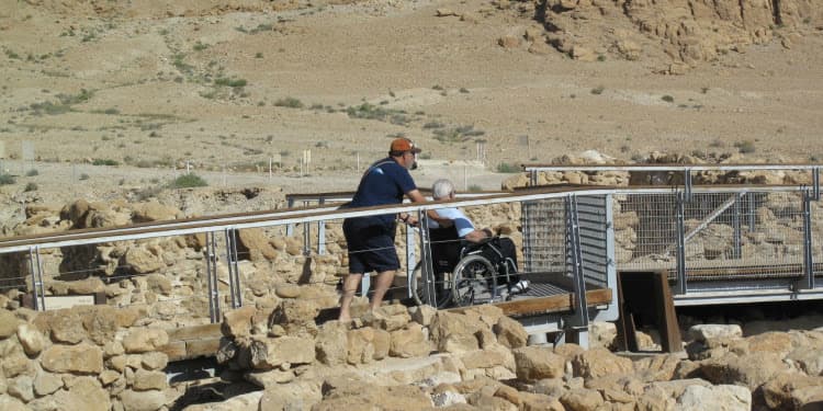 Man pushing a person in a wheel chair over a bridge.