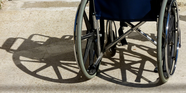 Close up image of the wheels of a wheelchair with its shadow cast behind it.