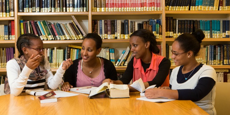 Group of four women sitting in a library together reading books.