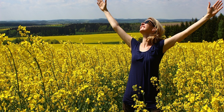 Woman lifting her hands up in praise while standing in a yellow flower field.