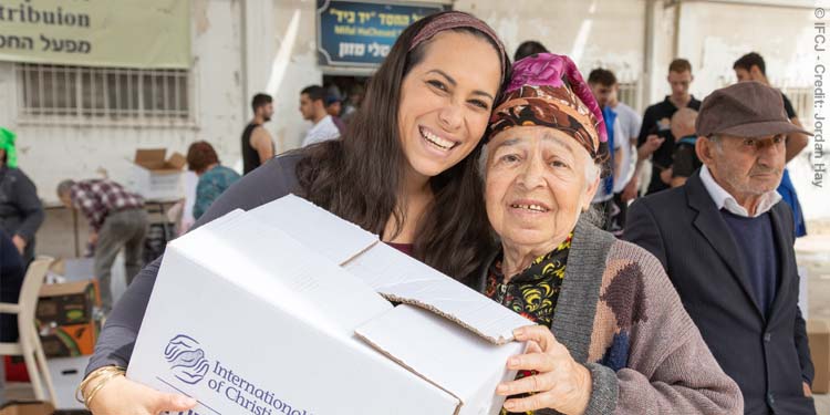 Yael Eckstein smiling with an elderly Jewish woman while holding an IFCJ food box.