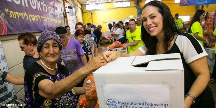 Yael Eckstein smiling while passing an IFCJ food box to an elderly Jewish woman.